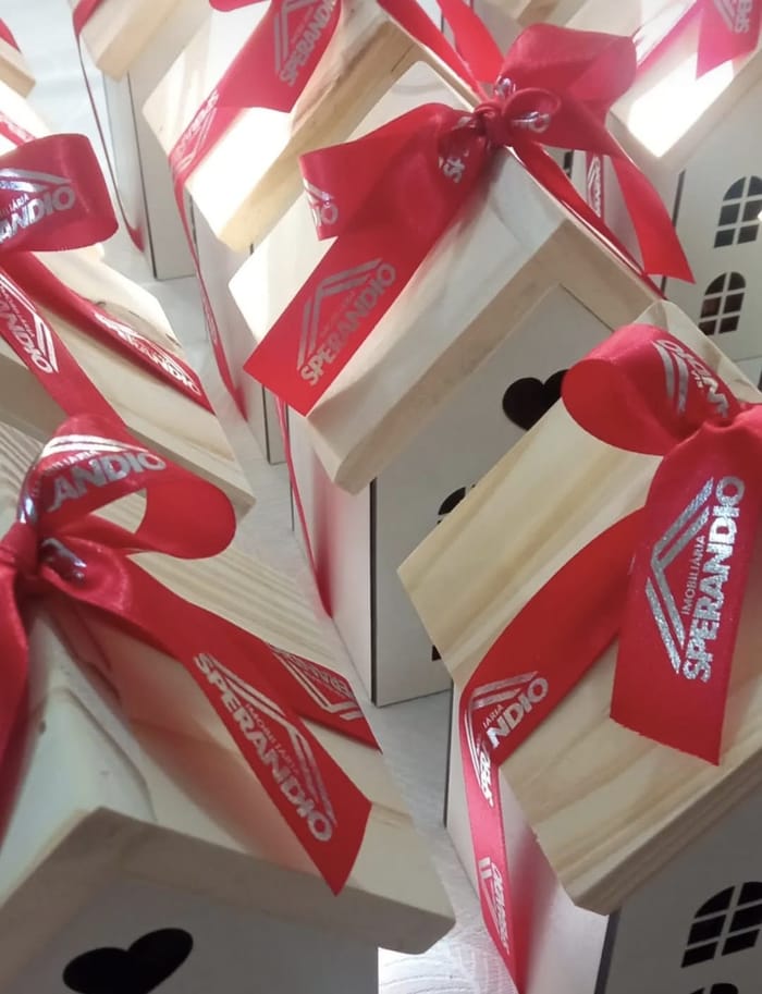 Casinhas de madeira com laço de fita vermelha estampada com o logotipo da empresa cliente