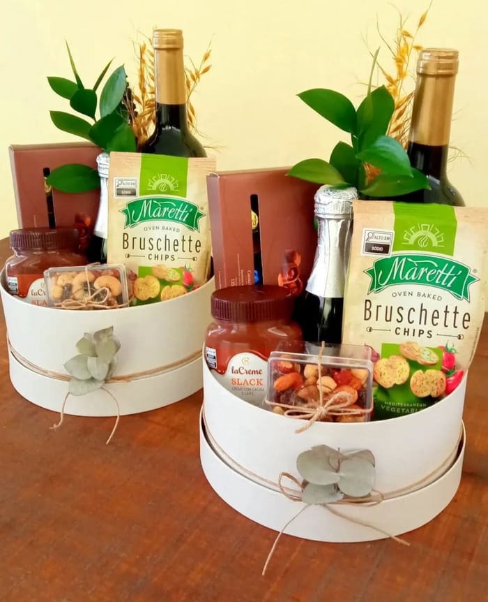 Duas caixas redondas creme com vinho, espumante, bruschettas, creme de avelã e castanhas, decoradas com eucalipto